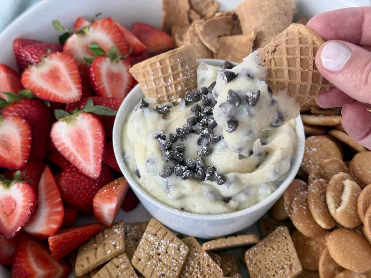 cannoli dip in bowl topped with chocolate chips waffle cone pieces cut strawberries and cookies for dipping