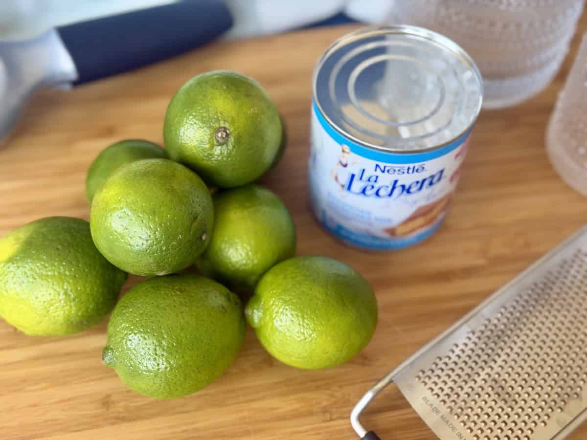 fresh whole limes can of sweetened condensed milk microplane on wood cutting board