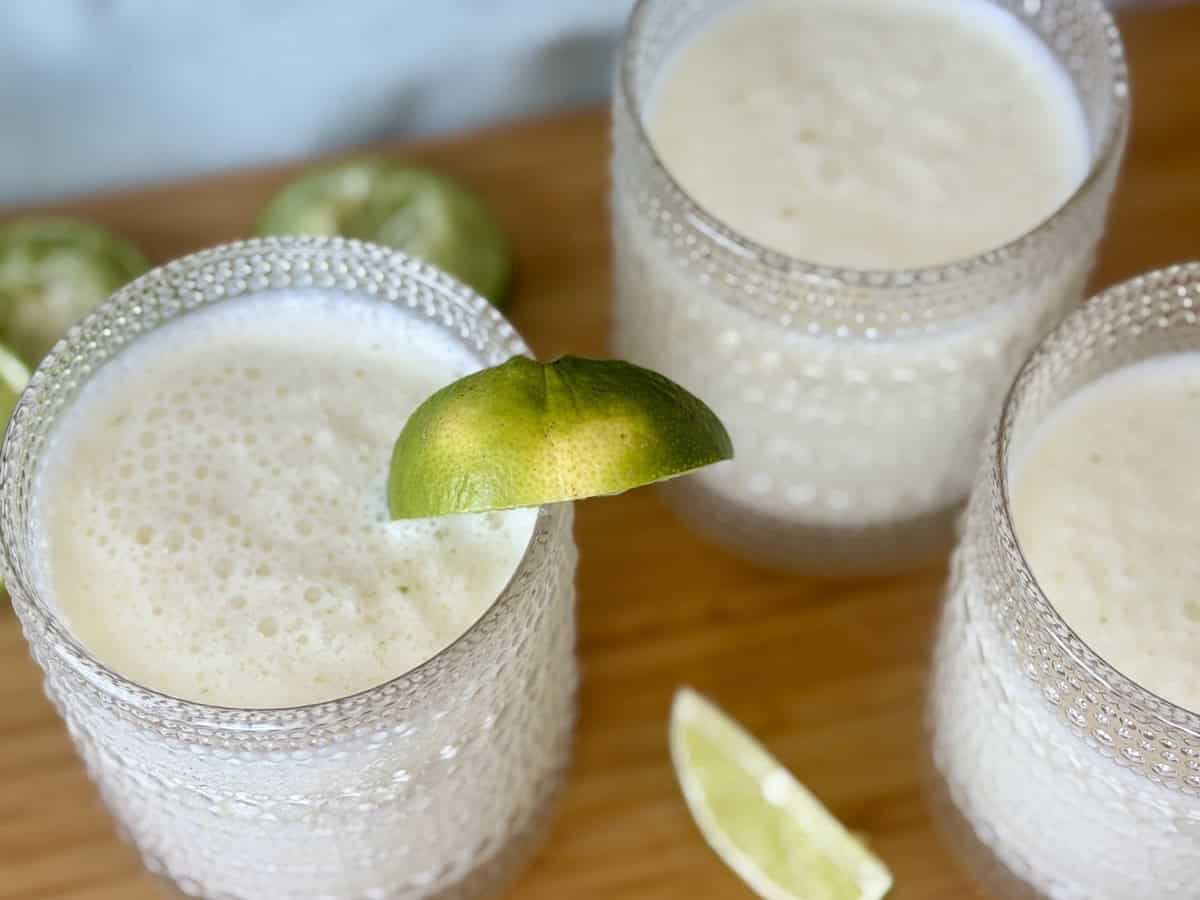 3 glasses of Brazilian lemonade garnished with lime wedges on wood cutting board