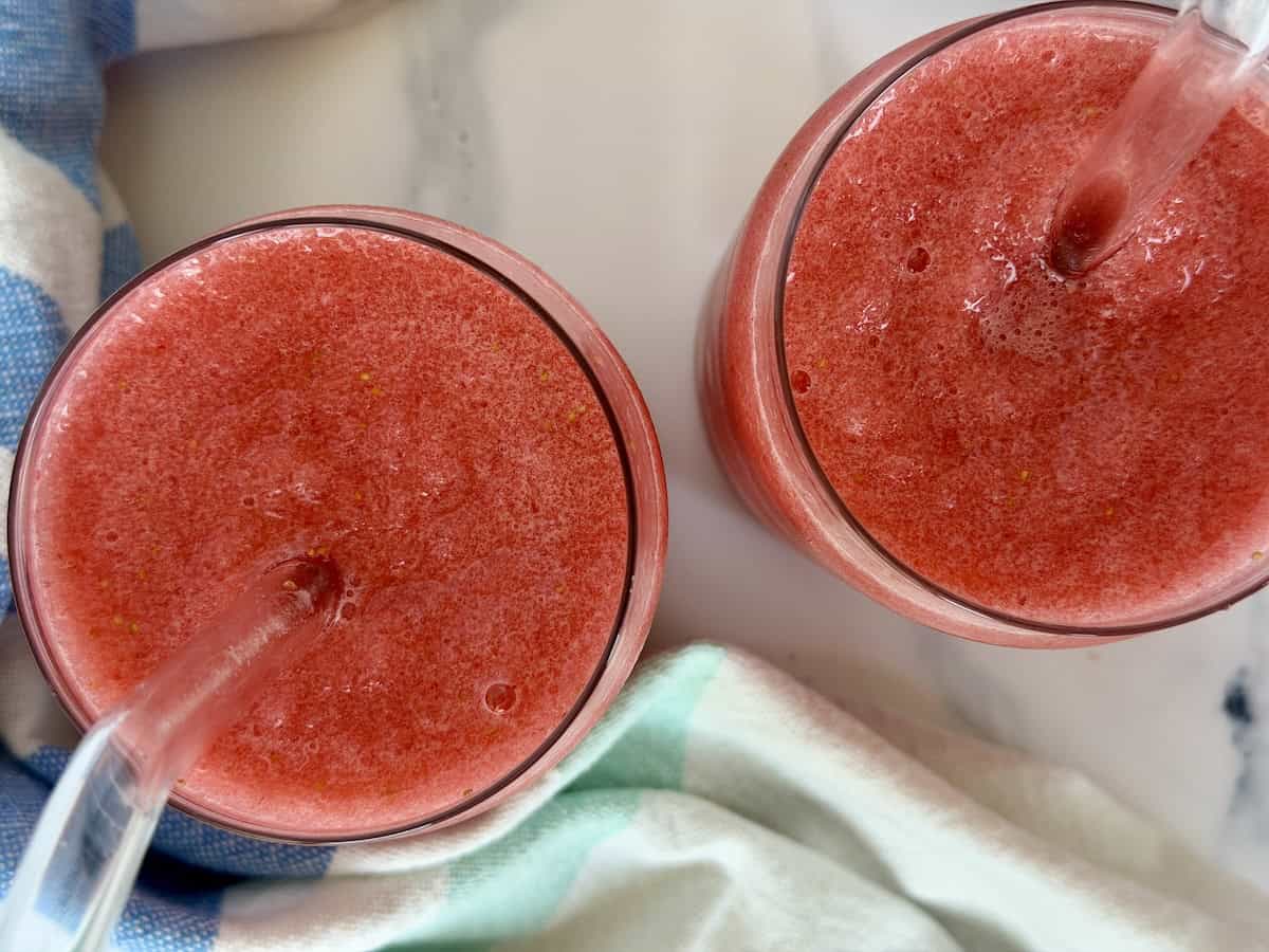 two strawberry slushies in glasses with big straws