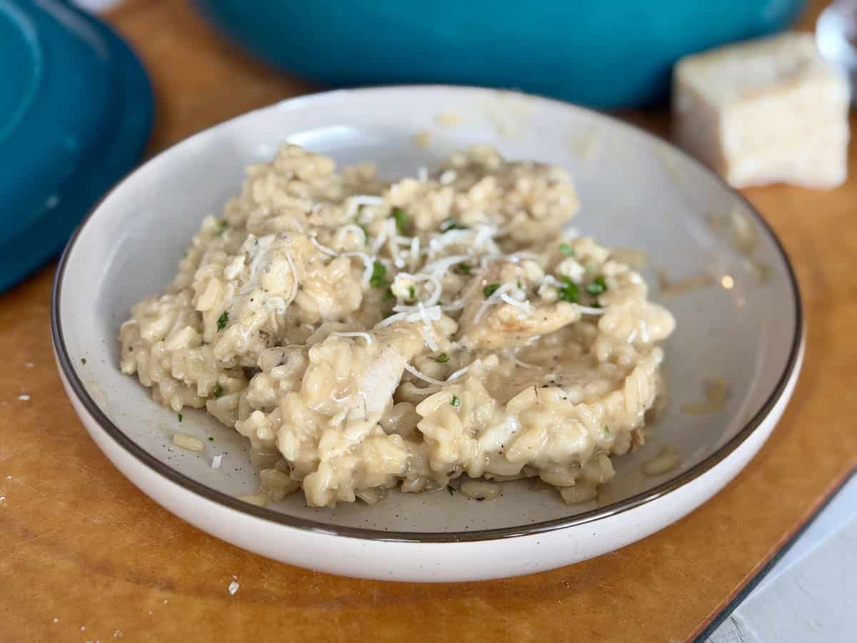 plate of chicken marsala risotto on wood cutting board block of parmesan cheese