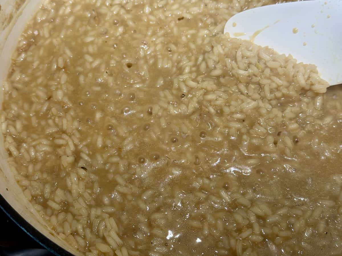 bubbling risotto cooking in enameled dutch oven stirring with white spatula