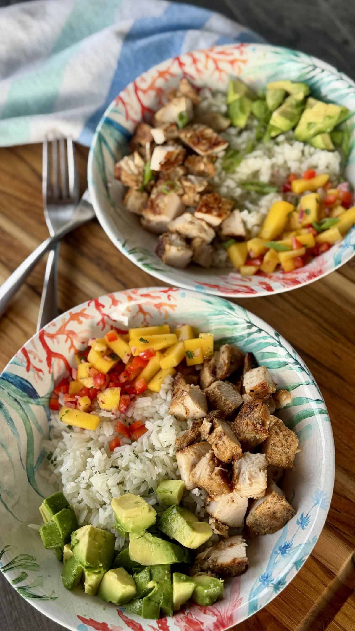 two jerk chicken rice bowls on wood cutting board with tropical kitchen towel