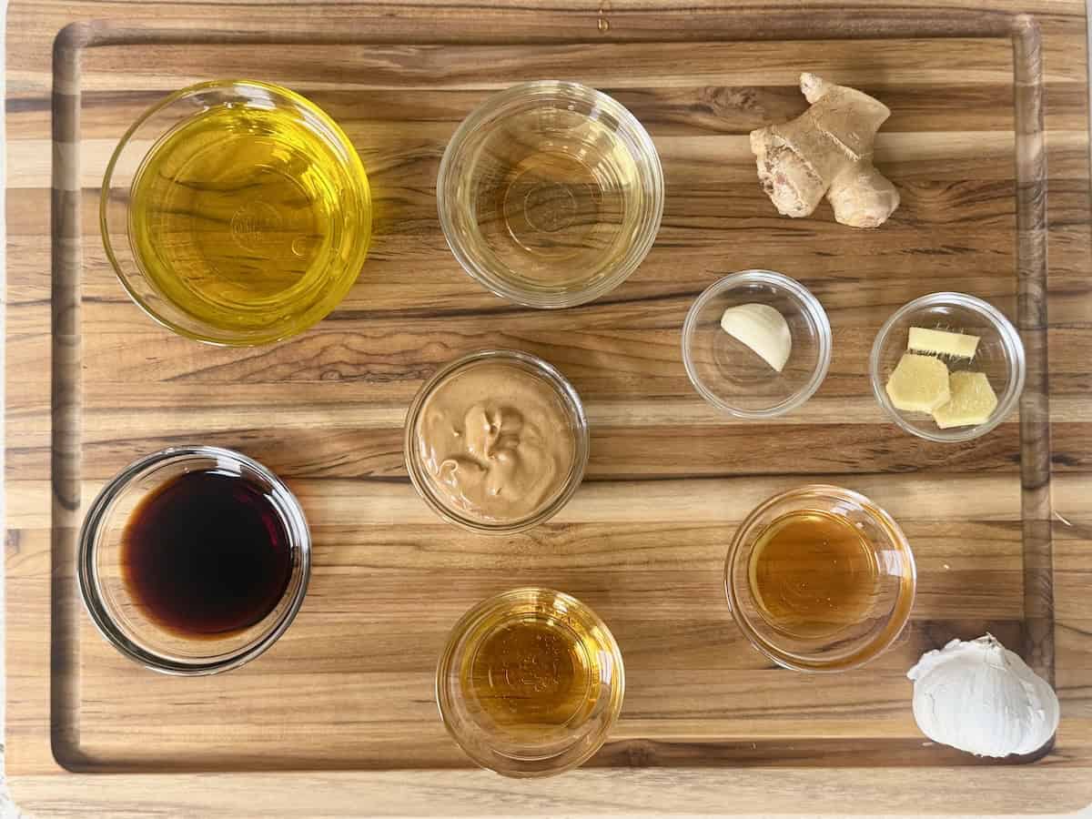 Thai dressing ingredients measured in small glass bowls on wood cutting board
