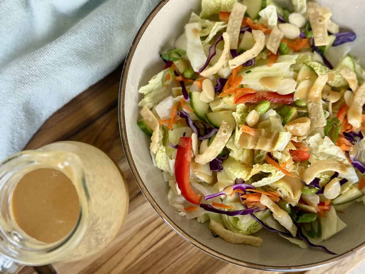 thai peanut salad dressing in glass jar next to bowl of salad on wood cutting board