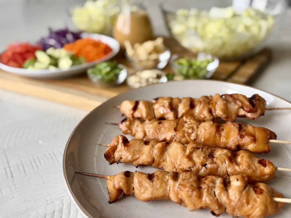thai chicken skewers on white plate next to salad ingredients