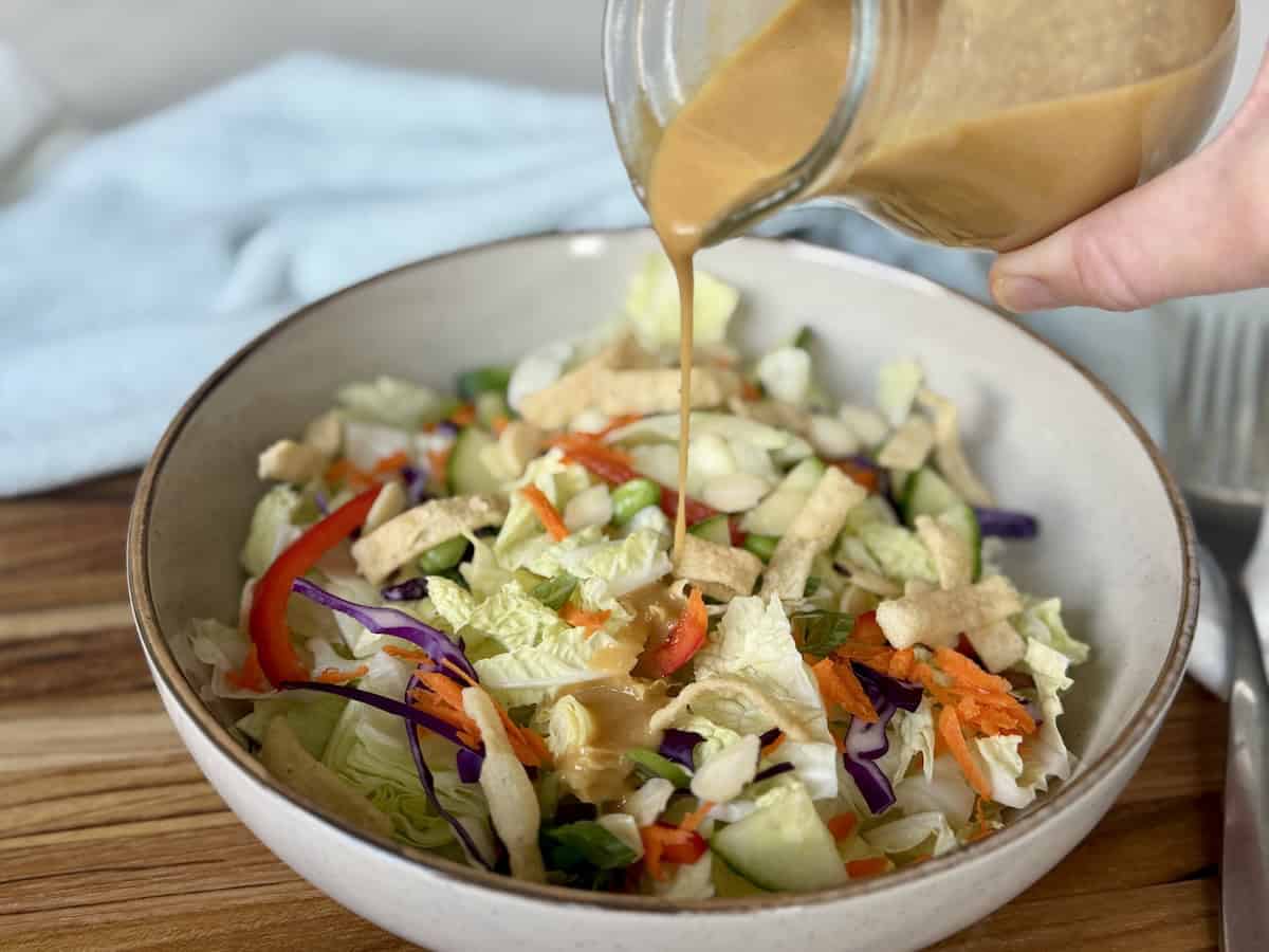 Thai peanut dressing pouring over salad in tan bowl