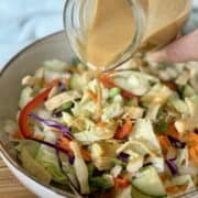 Thai peanut dressing pouring over salad in tan bowl
