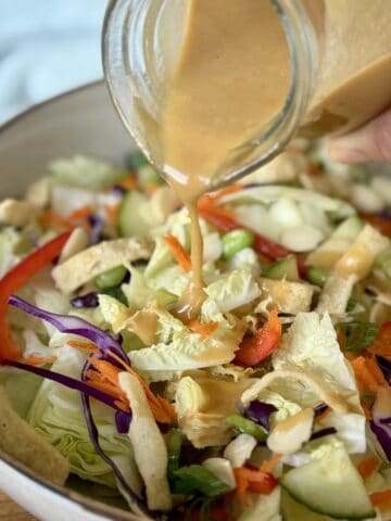 Thai peanut dressing pouring over salad in tan bowl